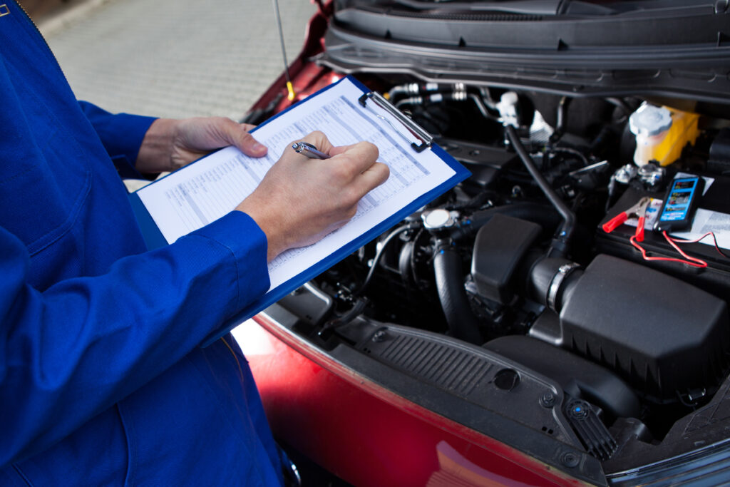 Service mechanic working on clipboard with hood of commercial vehicle open